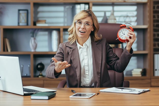 Photo mature businesswoman with alarm clock displaying time management in modern office