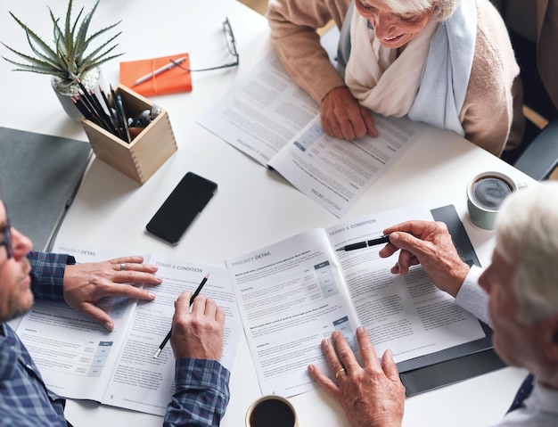 A mature couple meeting with a financial advisor to discuss retirement plans from above A senior couple meeting a banker to sign contracts together A mature couple reading and signing documents