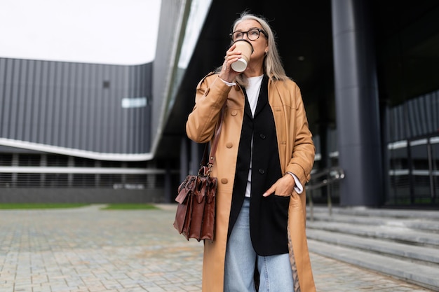 Mature elderly woman with a cup of coffee in her hands at the mall outside