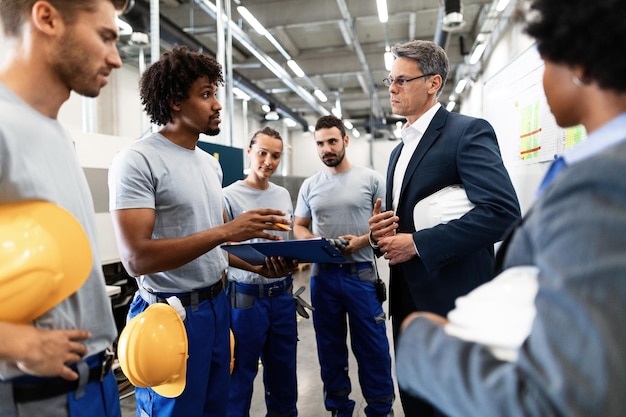 Mature engineer having a meeting with his employees and communicating about production reports in a factory