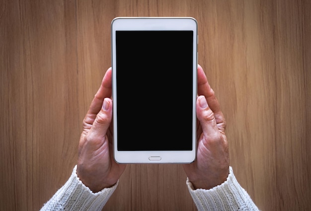 Mature female hands holding the white tablet pc computer with blank screen isolated on desk background