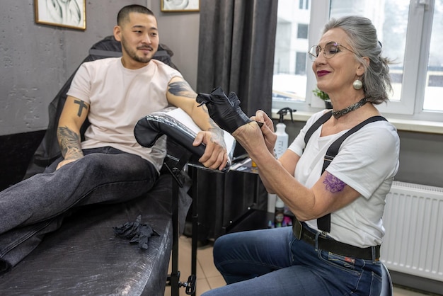 Mature female tattoo master working with the customer