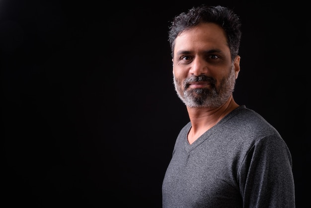  mature handsome bearded Indian man with curly hair against black wall