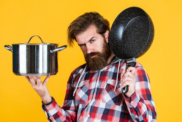 Mature handsome man in checkered shirt hold pan for cooking food, technology.