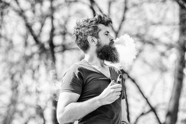 Mature hipster with beard hipster man hold vaping device Health safety and addiction inhaling vapor smoking ecigarette Bearded brutal male smoking electronic cigarette Portrait of masculinity