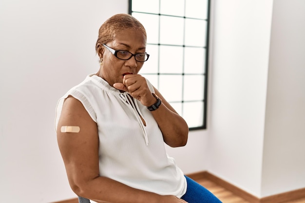 Mature hispanic woman getting vaccine showing arm with band aid feeling unwell and coughing as symptom for cold or bronchitis health care concept