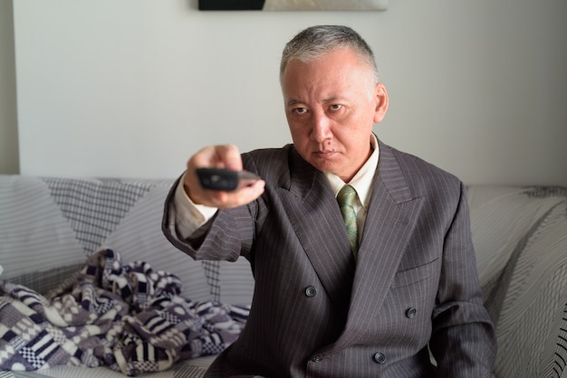 Mature Japanese businessman watching tv in the living room at home