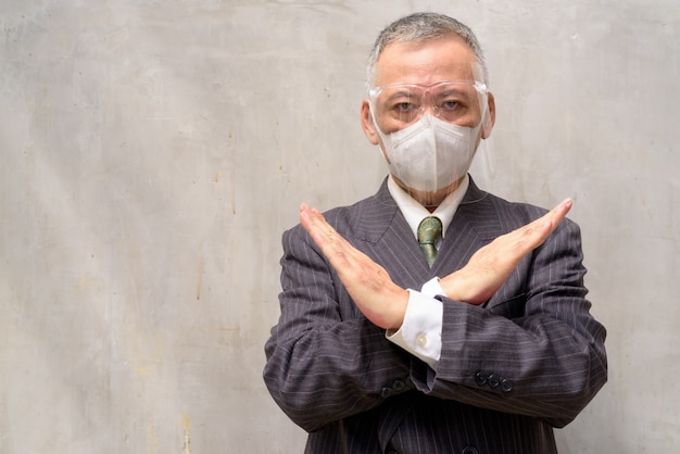 Mature Japanese businessman with mask and face shield showing stop gesture