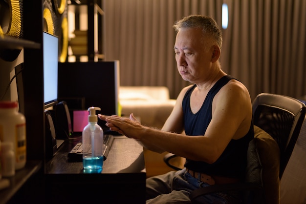 Mature Japanese man using hand sanitizer while working from home