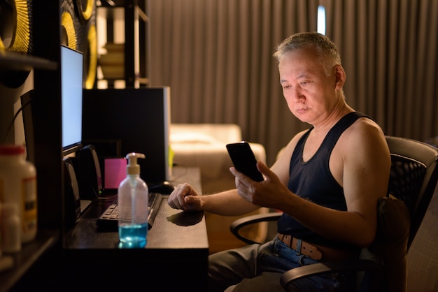 Mature Japanese man using phone while working from home