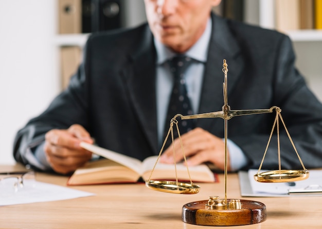 Mature male lawyer reading book with justice scale over the desk