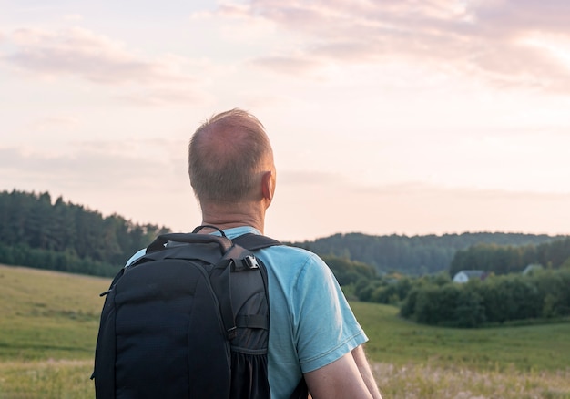 Mature man backpacker standing and enjoying cloudy sunset sky view solo hiker with backpack looking ...