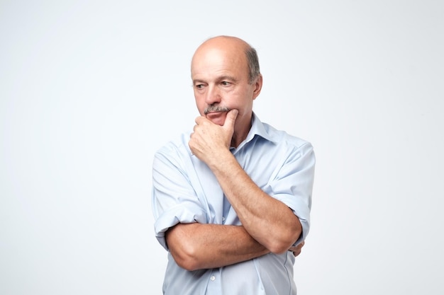 Mature man in blue shirt thinking and looking puzzled