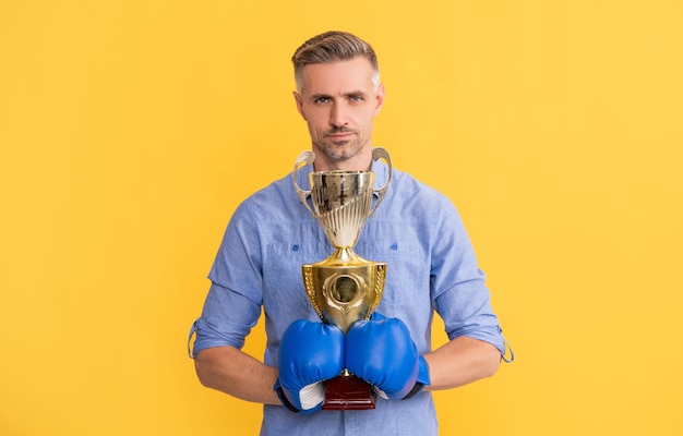 Photo mature man in boxing gloves hold champion cup on yellow background success