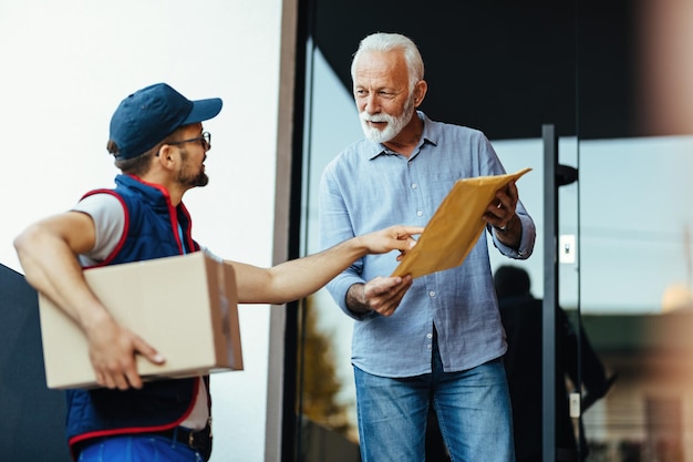 Mature man communicating with a deliverer while standing at front door and receiving a package