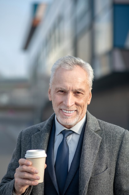 Mature man in elegant coat smiling nicely while having coffee