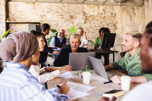 Mature man experienced in marketing strategy explaining to the work team the process of communication and advertising people working in the world of fashion and design