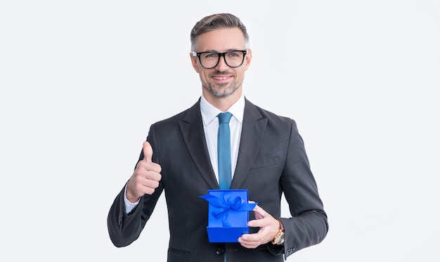 Mature man in eyeglasses and suit hold present box isolated on white background thumb up