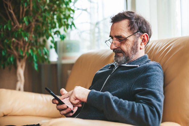 Mature man in glasses texting or messaging or searching or reading on a modern smartphone Seniors using technology concept