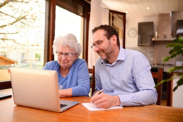 Mature man helping elderly senior woman at home with paperwork and computer internet lesson