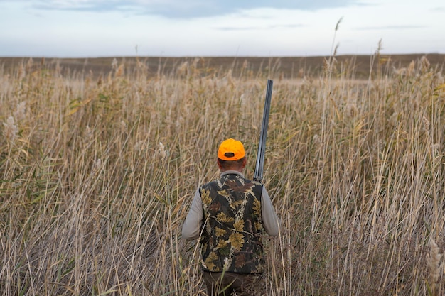 Mature man hunter with gun while walking on field