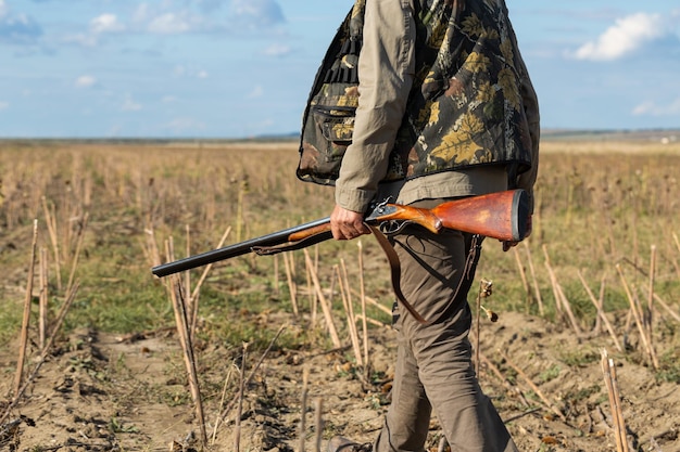 Mature man hunter with gun while walking on field