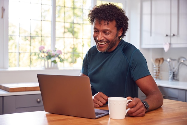 Mature Man In Kitchen Working From Home On Laptop Computer