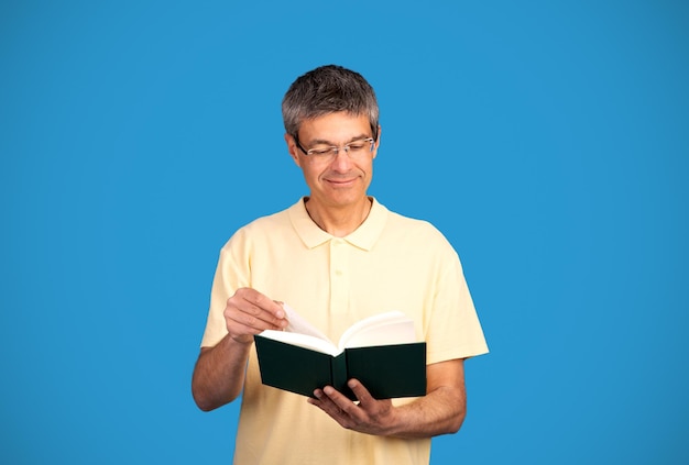 Mature man reading a book wearing eyeglasses on blue background