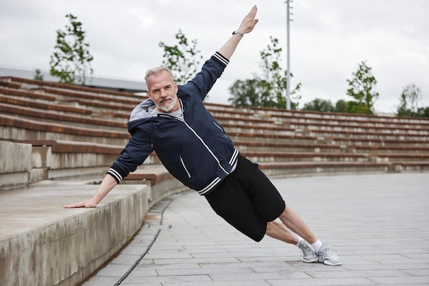 Photo mature man in side plank training core muscles at city park