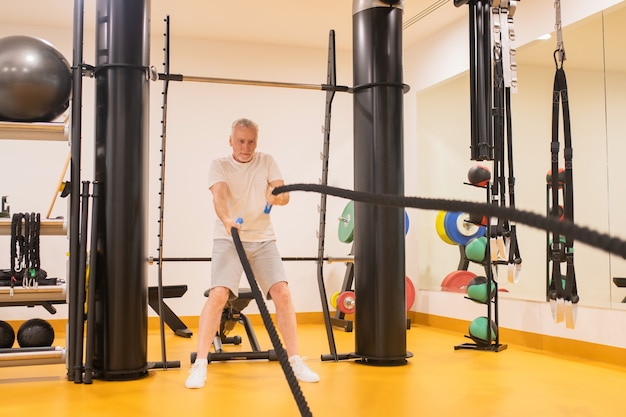 Mature man in sportswear pulling the ropes in gym