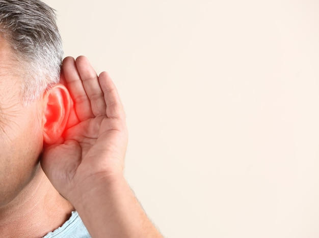 Mature man suffering from earache on light background closeup Space for text