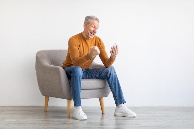 Mature man using cell phone celebrating success shaking fists