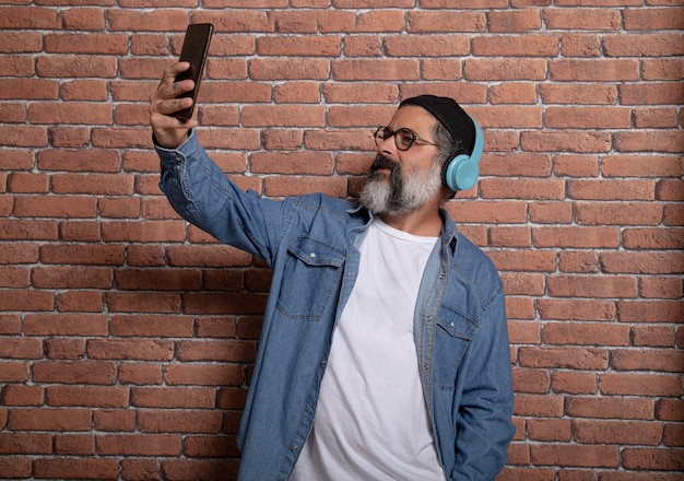 Mature man using a smartphone app with headphones. Mature fashionable man having fun with new technology trends - Technology concept.