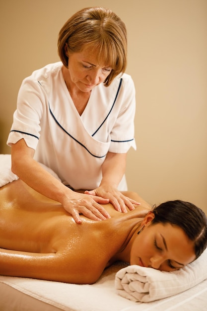 Mature massage therapist massaging back of young woman at the spa salon