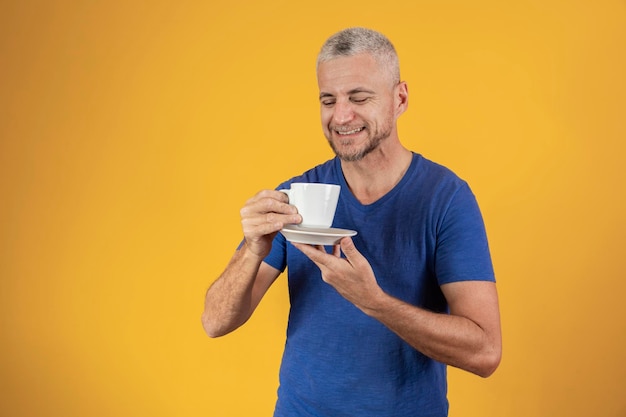 Mature middle aged man having a coffee or tea on yellow background with free space for text