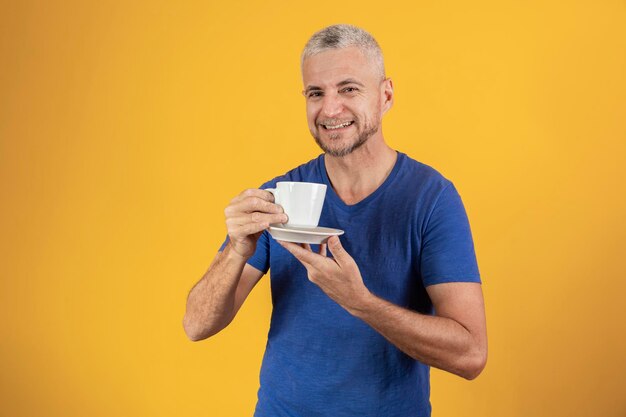 Mature middle aged man having a coffee or tea on yellow background with free space for text