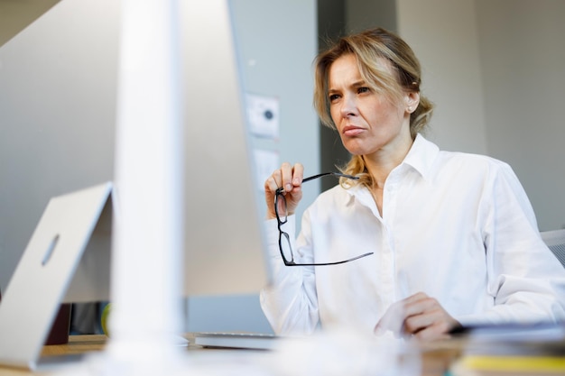 Mature pensive business woman with a worried expression works at a computer in the office