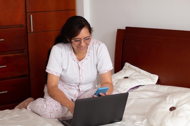 Mature productive 52yearold woman who uses her laptop and smartphone to work from bed