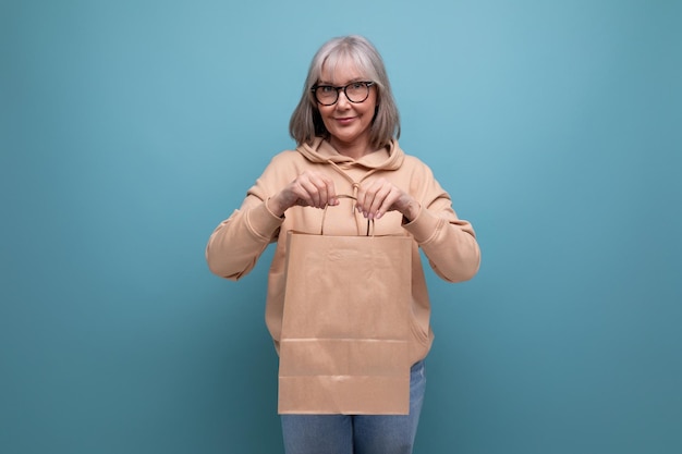 Mature s business woman with gray hair holding craft shopping bag on studio background with copy