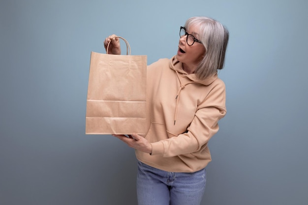 Mature s business woman with gray hair holding craft shopping bag on studio background with copy