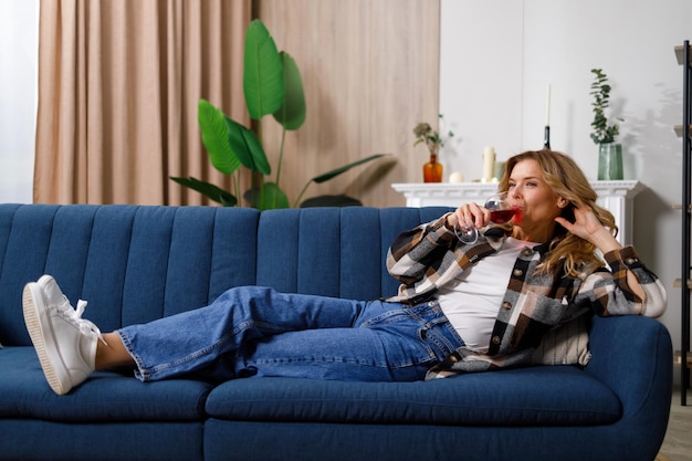 Mature saucasian woman lying on sofa and drinking red wine