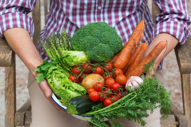 Mature senior woman holding in hands harvest from her orchard Assortment of ripe homegrown vegetables in farmer hands Organic market gardening bio food delivery zero waste ecofriendly concept