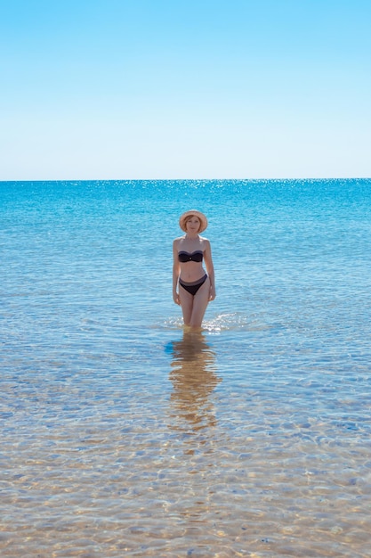 Mature slender woman in a swimsuit comes out of the water on a sunny day Summer vacation at the sea