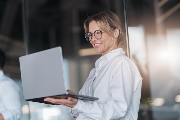 Mature smiling businesswoman at modern office working on laptop