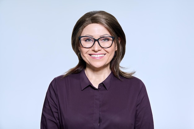 Mature smiling woman in glasses looking at camera on light background