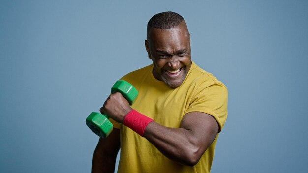 Mature strong athletic man coach pumping biceps with dumbbell in studio on gray background doing