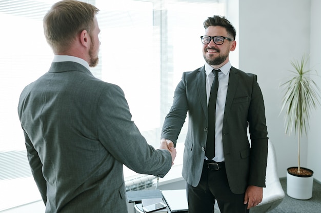 Mature successful businessman in formalwear looking at his business partner during handshake after negotiating and signing contract