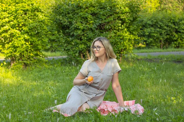 Mature woman in glasses is resting in the park Eating an apple on a green lawn in the shade