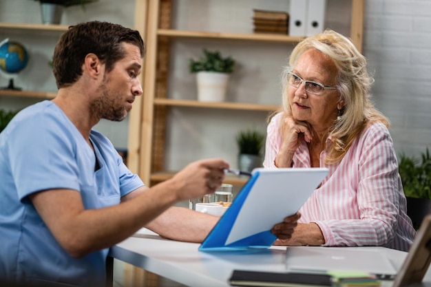 Mature woman and her doctor going through medical documents during the appointment at doctor's office Focus is on woman