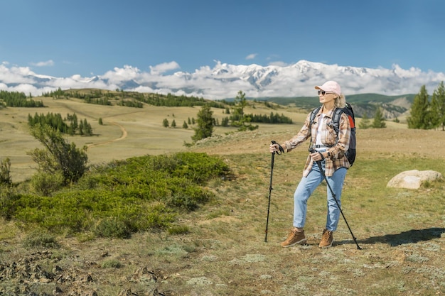 Mature woman hiker with backpack using poles hiking in mountains